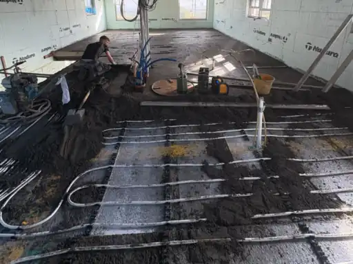 Screed being pumped over underfloor heating pipes in a large room